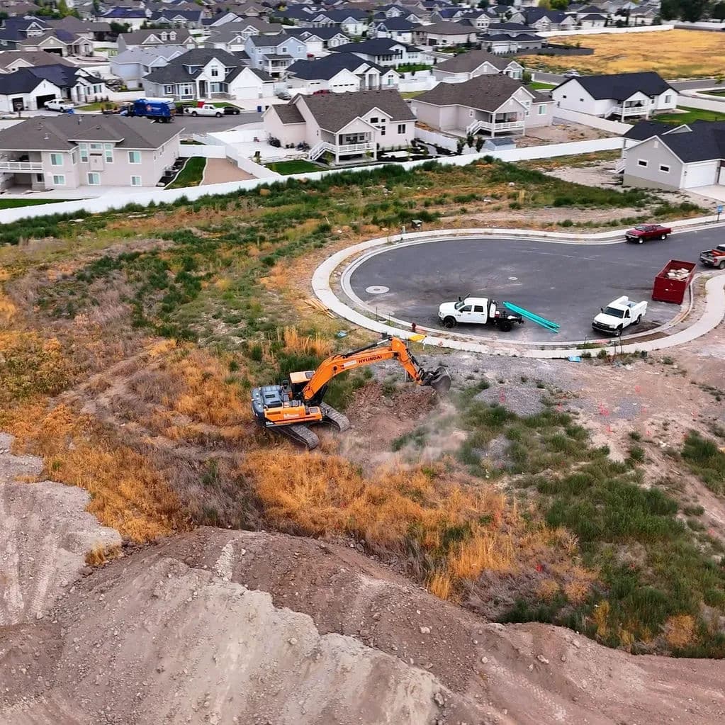 Excavator digging near suburban homes and a circular road in residential construction area.