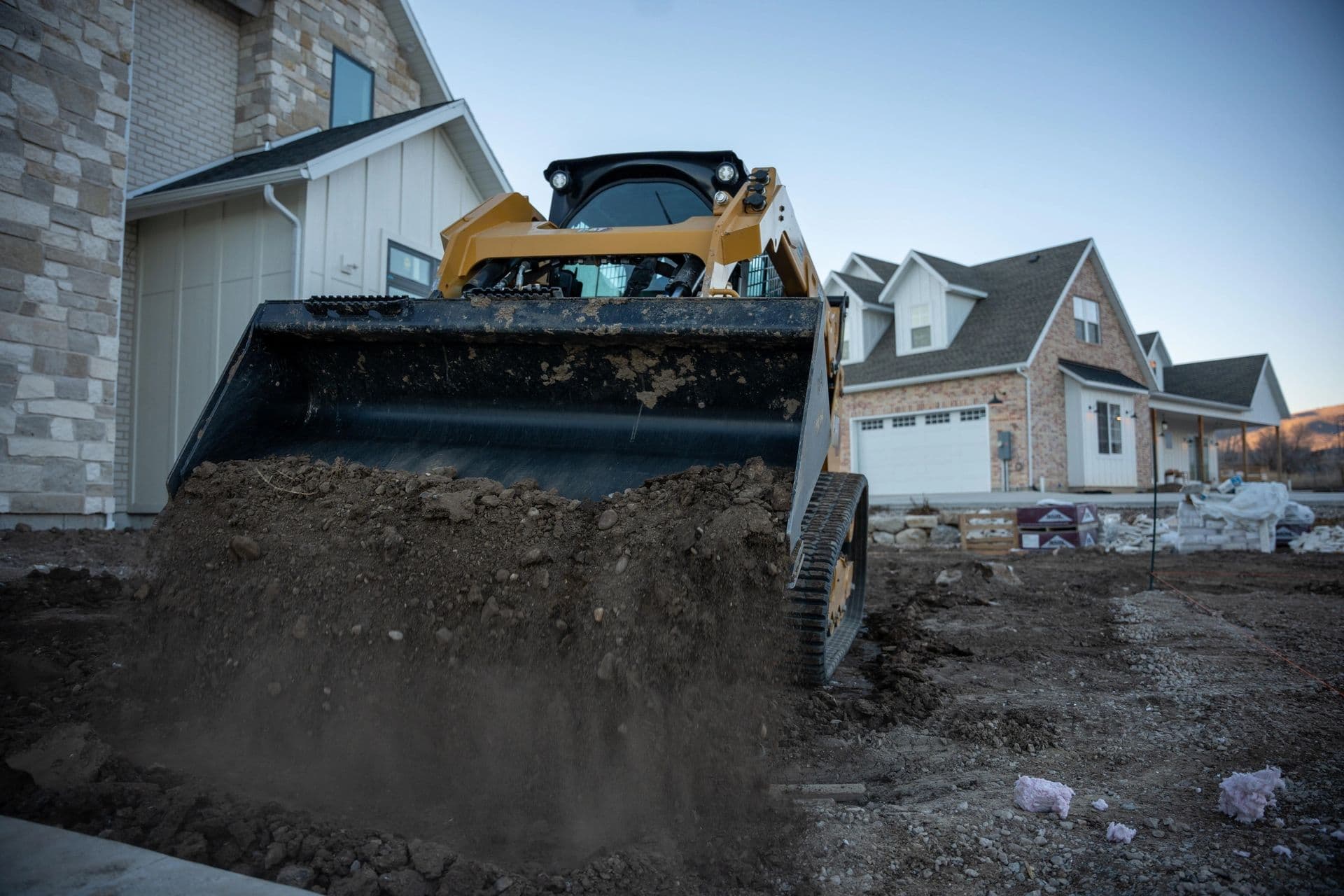 Bulldozer scooping dirt at residential construction site with houses in background.